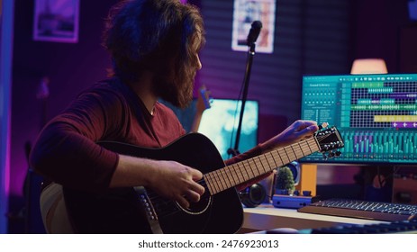 Music producer tuning his acoustic guitar before playing instrument, recording and mixing tunes to create new soundtracks. Singer composing a song using electronic panel controls. Camera B. - Powered by Shutterstock