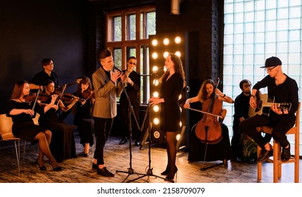 Music rock band with string quartet on the background of the loft interior sing and play instruments