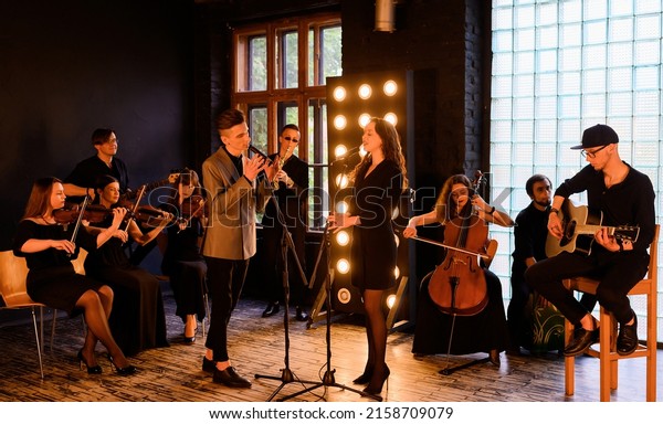 Music rock band with\
string quartet on the background of the loft interior sing and play\
instruments