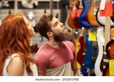 Music, Sale, People, Musical Instruments And Entertainment Concept - Happy Couple Of Musicians Choosing Guitar At Music Store