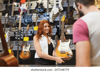 Music, Sale, People, Musical Instruments And Entertainment Concept - Assistant Showing Electric Guitar To Customer At Music Store