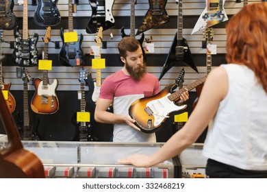 Music, Sale, People, Musical Instruments And Entertainment Concept - Assistant Showing Electric Guitar To Customer At Music Store