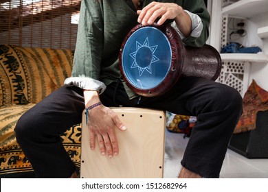 Music shot of a white man playing cajon drum box and arabic darbuka at the same time on an alternative house studio background. Having fun experimenting with exotic instruments at home.
