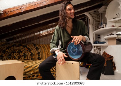 Music shot of a young handsome man playing cajon drum box and arabic darbuka at the same time on an alternative house studio background. Having fun experimenting with exotic instruments at home.
