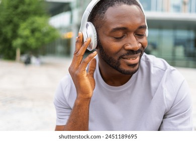 Music song concept. Good start day. Happy African American man listening modern hit on street in city. Person guy wearing headphones enjoy listening favorite music outdoor. People lifestyle joy - Powered by Shutterstock