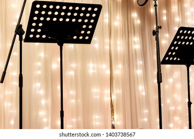 Music Stands In Front Of A Semi Opaque Curtain Covering Strings Of Starry Lights