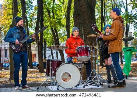 Music street performers with girl violinist on autumn outdoor. Group people three men and women with music instrument in park.