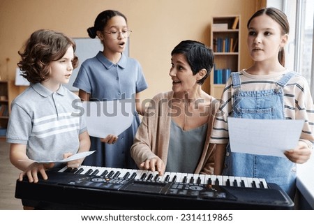 Music teacher singing songs together with children while playing piano in music class