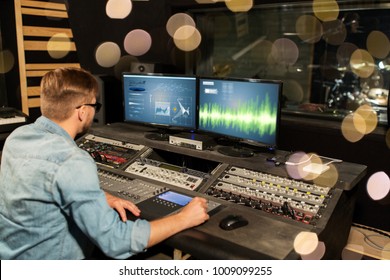 music, technology, people and equipment concept - man at mixing console in sound recording studio over lights