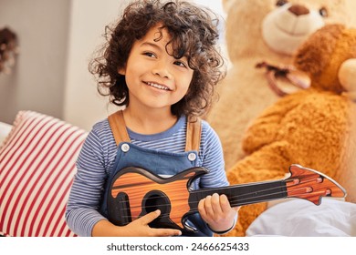 Music, thinking and toy guitar with boy in bedroom of home for instrument fun or practice. Idea, learning and smile with happy child playing pretend musician on sofa in apartment to relax for weekend - Powered by Shutterstock