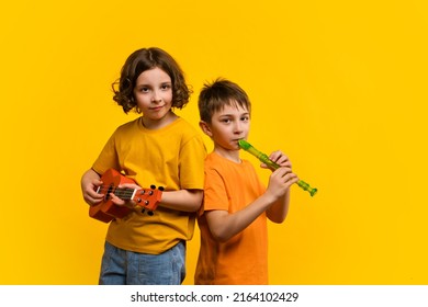 Musical duet in studio on yellow background. Child girl plays ukulele. School boy plays block flute. Two school children practice playing musical instruments - Powered by Shutterstock