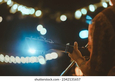 Musical and enjoyment concepts. Rear view of the man sitting play acoustic guitar on the outdoor concert with a microphone stand in the front. - Powered by Shutterstock