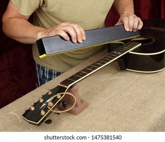 Musical Instrument Guitar Repair And Service - Worker Grinds Black Guitar Neck Frets.