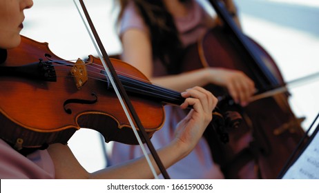 Musical Orchestra Of Female Musicians Plays On The Summer Terrace Outside, Hands Holding A Violin And Bow, Close Up