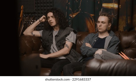 Musical rock band sits on couch. Stylish male musicians, artists, performers listen to ready recorded songs for new album in professional sound and music recording studio. Concept of music production. - Shutterstock ID 2291683337
