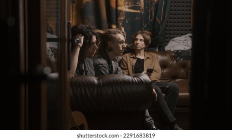 Musical rock band sits on sofa. Young male musicians, artists, performers listen to finished recorded songs for new album in professional sound and music recording studio. Concept of music production. - Shutterstock ID 2291683819