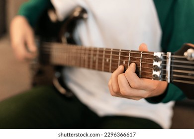 Musical Talent. Closeup Of Guy's Hands Playing Chords On Electric Guitar, Holding Instrument And Touching Strings Sitting Indoor. Music Hobby And Leisure. Cropped Shot, Selective Focus
