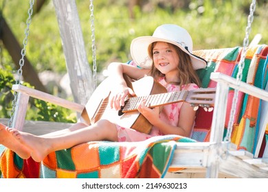 Musician Child Playing Guitar. Kid Girl Singing And Playing Guitar Outside. Summer Activity For Children In Warm Weather. Cute Little Girl Having Fun On A Swing In Beautiful Summer Garden.