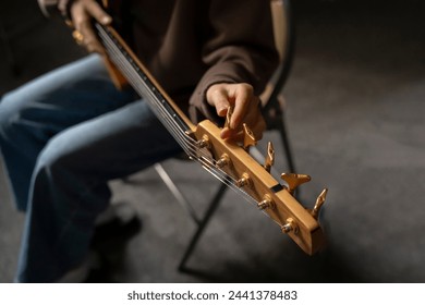 Musician Fine-Tuning Acoustic Guitar Strings in a Dimly Lit Room of music studio - Powered by Shutterstock