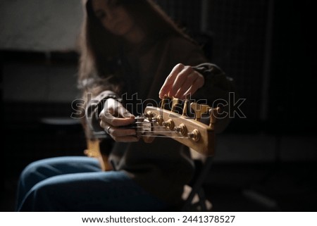 Musician Fine-Tuning Acoustic Guitar Strings in a Dimly Lit Room of music studio