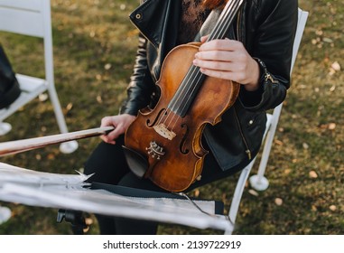 A Musician Girl Sits On A Chair, Holds A Violin And Prepares For A Recital.