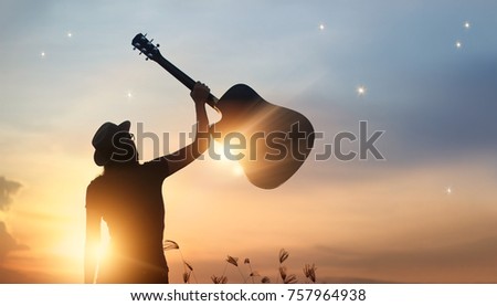 

Musician holding guitar in hand of silhouette on sunset nature background