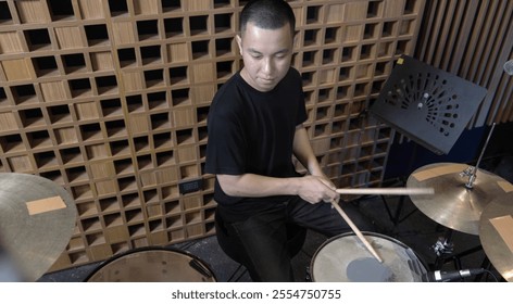 Musician playing a drum set in a professional recording studio with acoustic paneling and recording equipment in the background. The scene captures the essence of live music production and creativity  - Powered by Shutterstock