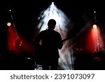 Musician playing guitar performing on stage under spot light. Silhouette of a music artist and band on stage.