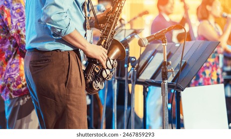 Musician playing saxophone on blurred background. Man with friends blow saxophone with the band for performance. Music instrument played by saxophonist player musician in festival. Selective focus.