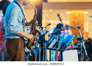 Musician playing saxophone on blurred background. Man with friends blow saxophone with the band for performance. Music instrument played by saxophonist player musician in festival. Selective focus.