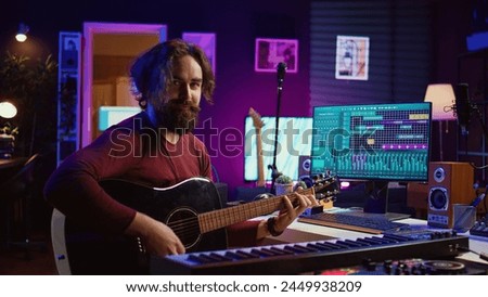 Musician plays acoustic guitar and records melody to compose new song and tunes. Computer screen showing DAW software interface with soundtracks, sound engineer in music production. Camera B.