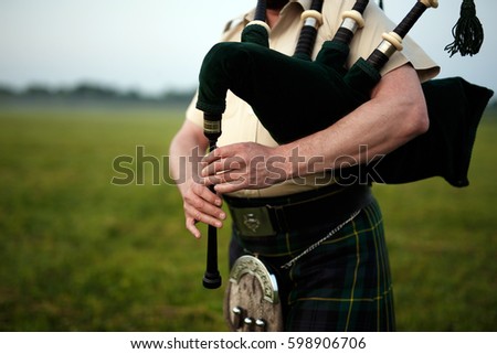 A musician plays the bagpipes in the fields. Fingers and bagpipe close up.