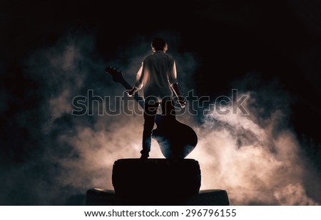The musician plays on a large rock guitar in a great smoke, rock music, concert and festival