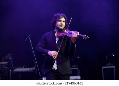 Musician violinist with a violin in his hands standing on stage during the concert. Around the bright light from the floodlights. 