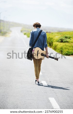 Musician, walking and man with a guitar on a road trip, journey or tour in the countryside on highway. Guitarist, travel or back of guy trekking on street or asphalt in a green and rural landscape