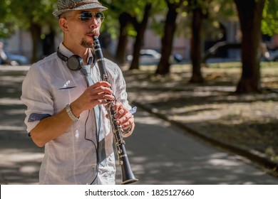 Musician wearing in titfer playing music with clarinet on a city sidewalk.