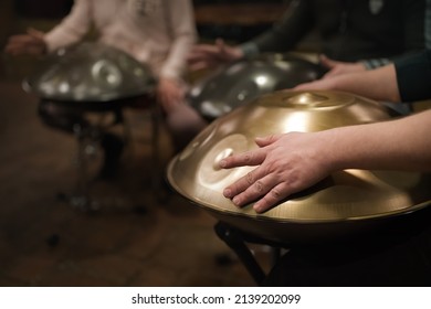 A musician's hand playing the handpan with other people. Handpan is a term for a group of musical instruments that are classified as a subset of the steelpan. 