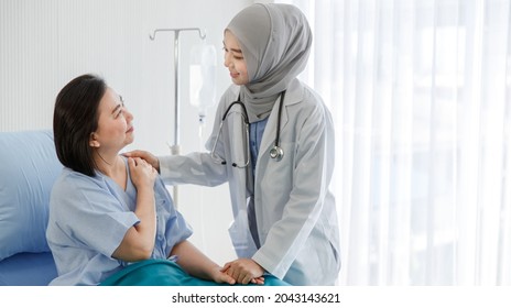 Muslim Arab Islam Female Doctor Wears Grey Hijab And White Lab Coat Uniform With Stethoscope Standing Visiting Encourage Cheering Up Old Asian Woman Patient On Hospital Bed With Normal Saline Pole.