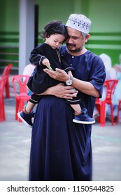 Muslim Asian baby boy on father shoulder holding bank note,a pocket money gift while they are visits to friends and family after morning prayers. Boy sweating during Muslim celebrated of Eid al-Adha. 
