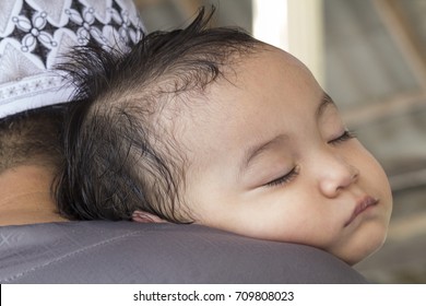 Muslim Asian Baby boy sleeping on father's shoulder.Boy sweating, tired and fallen to sleep during Muslim celebrated of Eid al-Adha. After morning prayers while they are visits to friends and family.