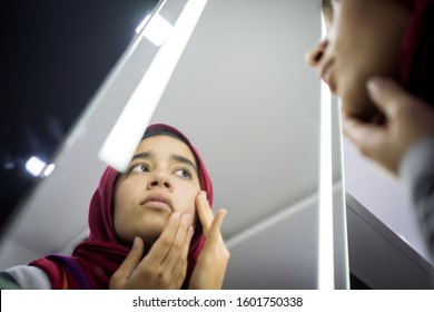 Muslim beautiful girl looking into mirror checking face skin