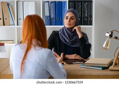 Muslim Boss Woman Listening To Employee's Report In Her Office. Arrogant Look And Self-confidence.