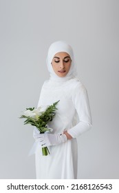 muslim bride in gloves and white dress holding calla lily flowers isolated on grey