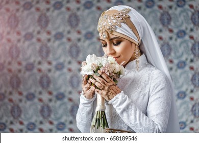 Muslim bride with jewelery in a headscarf hijab with a bouquet of flowers in a mosque