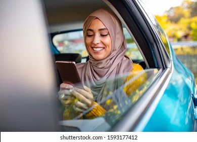 Muslim business woman in car. Writing a message on her mobile phone. Positive pensive Islamic woman in hijab sitting on backseat of taxi and drinking coffee while using gadget - Powered by Shutterstock