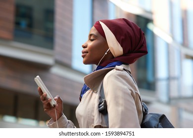 Muslim business woman using smartphone listening to music with headphones in city independent female wearing hijab headscarf - Powered by Shutterstock