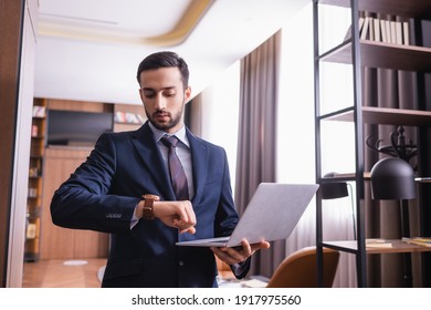 Muslim businessman looking at wristwatch and holding laptop in restaurant