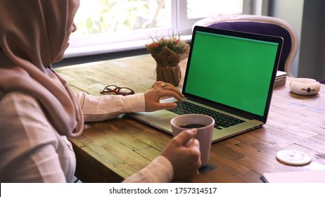Muslim Businesswoman Drinking Coffee In His Office And Reading Something On The Computer.Shot Of A Woman Typing On A Computer Laptop With A Key-green Screen.Woman Hand Typing Laptop With Green Screen
