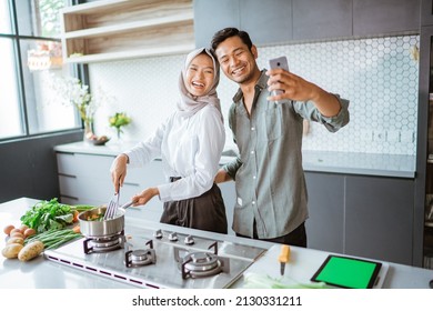 Muslim Couple Cooking Their Food In The Kitchen And Taking Selfie