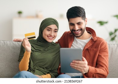 Muslim Couple Doing Online Shopping Via Digital Tablet Computer And Credit Card Sitting On Sofa At Home. Middle Eastern Spouses Browsing Internet Purchasing Something. E-Commerce And Technology - Shutterstock ID 2138369267